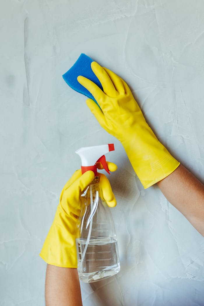 hero-img Hands in yellow gloves cleaning wall with sponge and spray bottle.